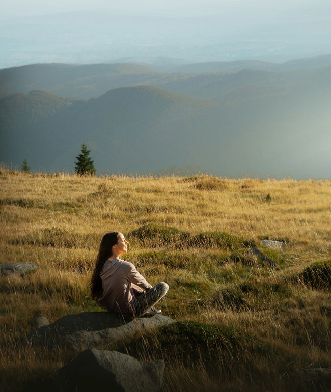 Frau sitzt entspannt auf einem Felsen und blickt über eine weite Landschaft