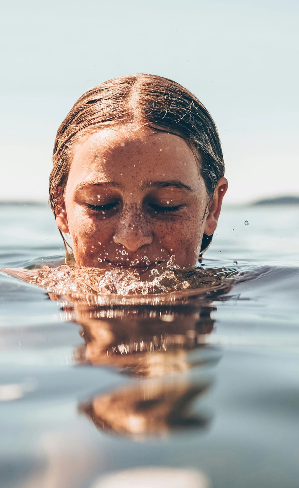 Frau taucht Gesicht ins Wasser in ruhiger Natur