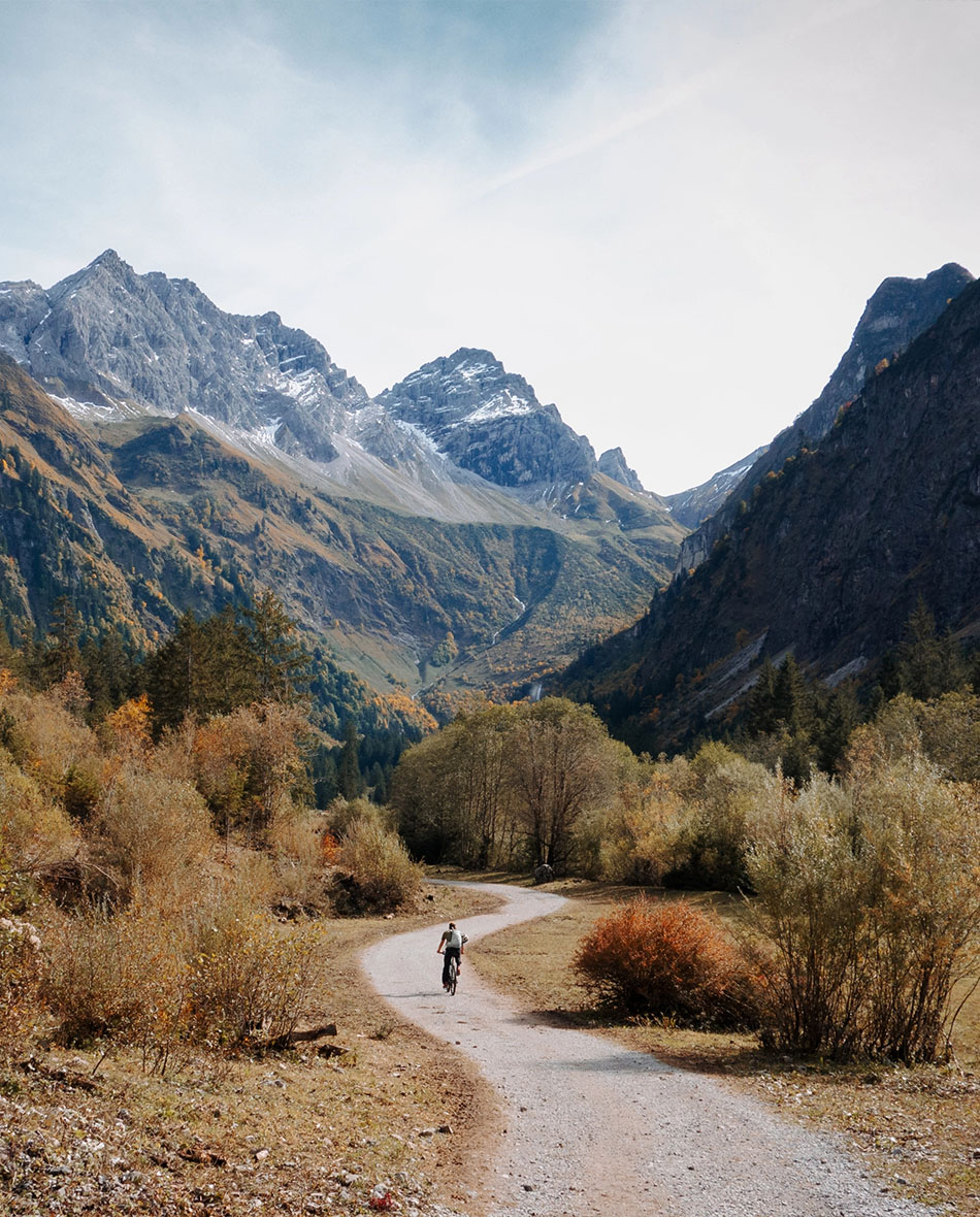 Radfahrer fährt auf einem Weg durch ein alpines Tal mit Bergpanorama